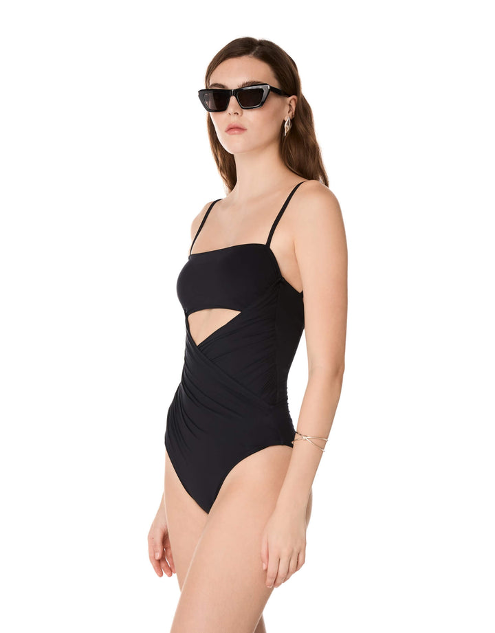 Kióhne Sierra black one-piece swimsuit with diagonal draped panels, bust cut-out and thin straps, styled with sunglasses