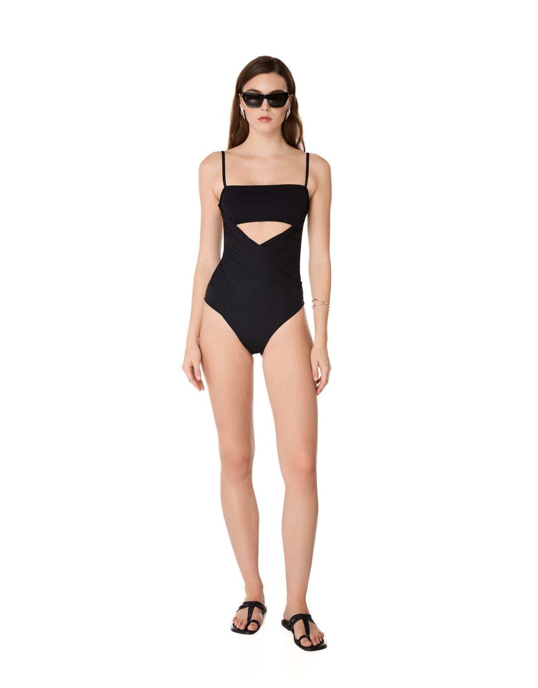 Kióhne Sierra black one-piece swimsuit with diagonal draped panels, bust cut-out and thin straps, styled with black sandals and sunglasses